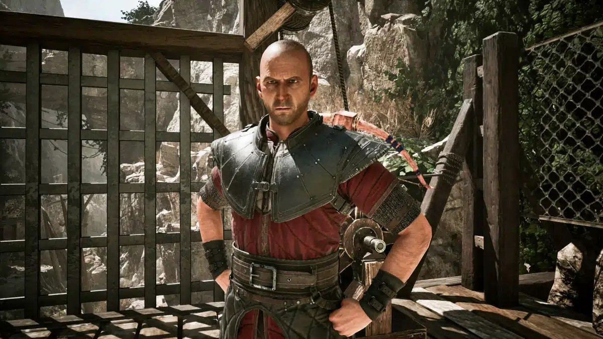 A man wearing a red and black outfit stands confidently in front of a wooden fence