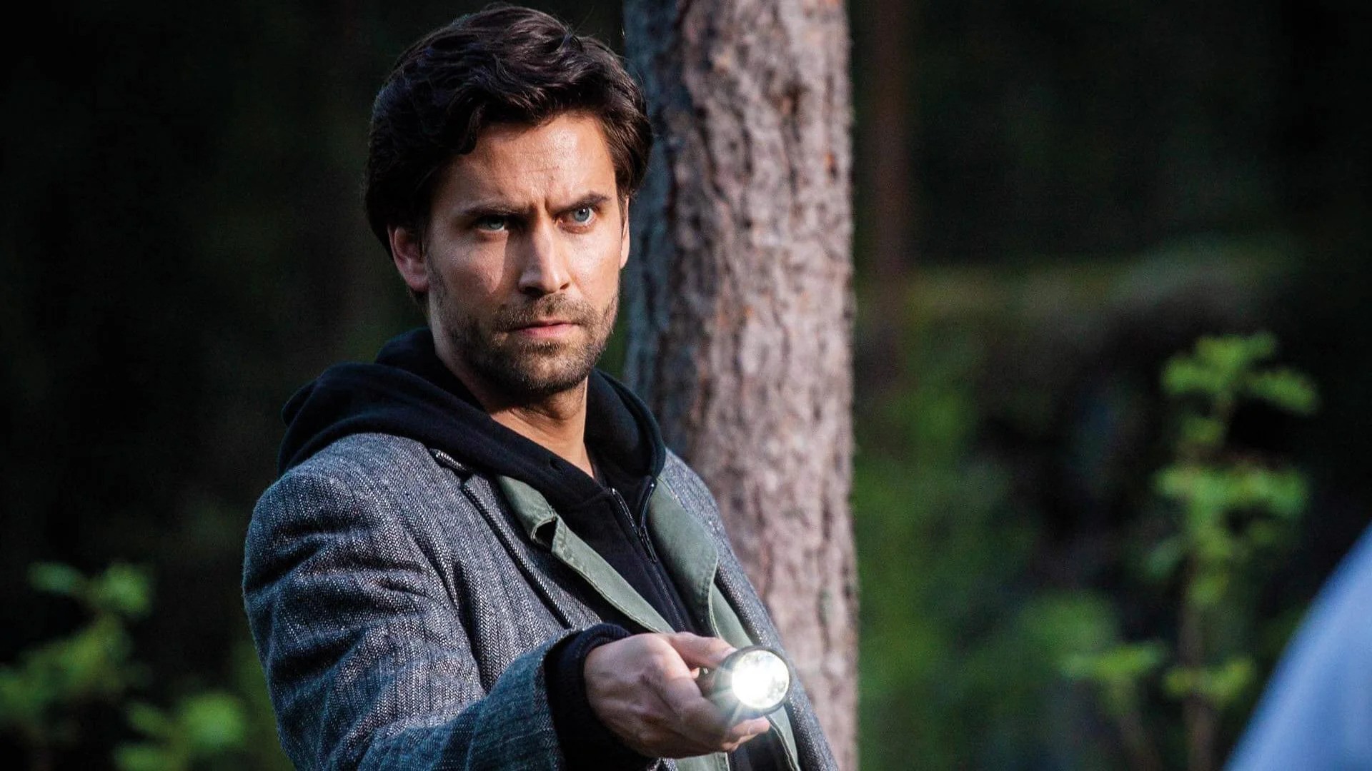 Alan Wake stands in the woods, holding a flashlight